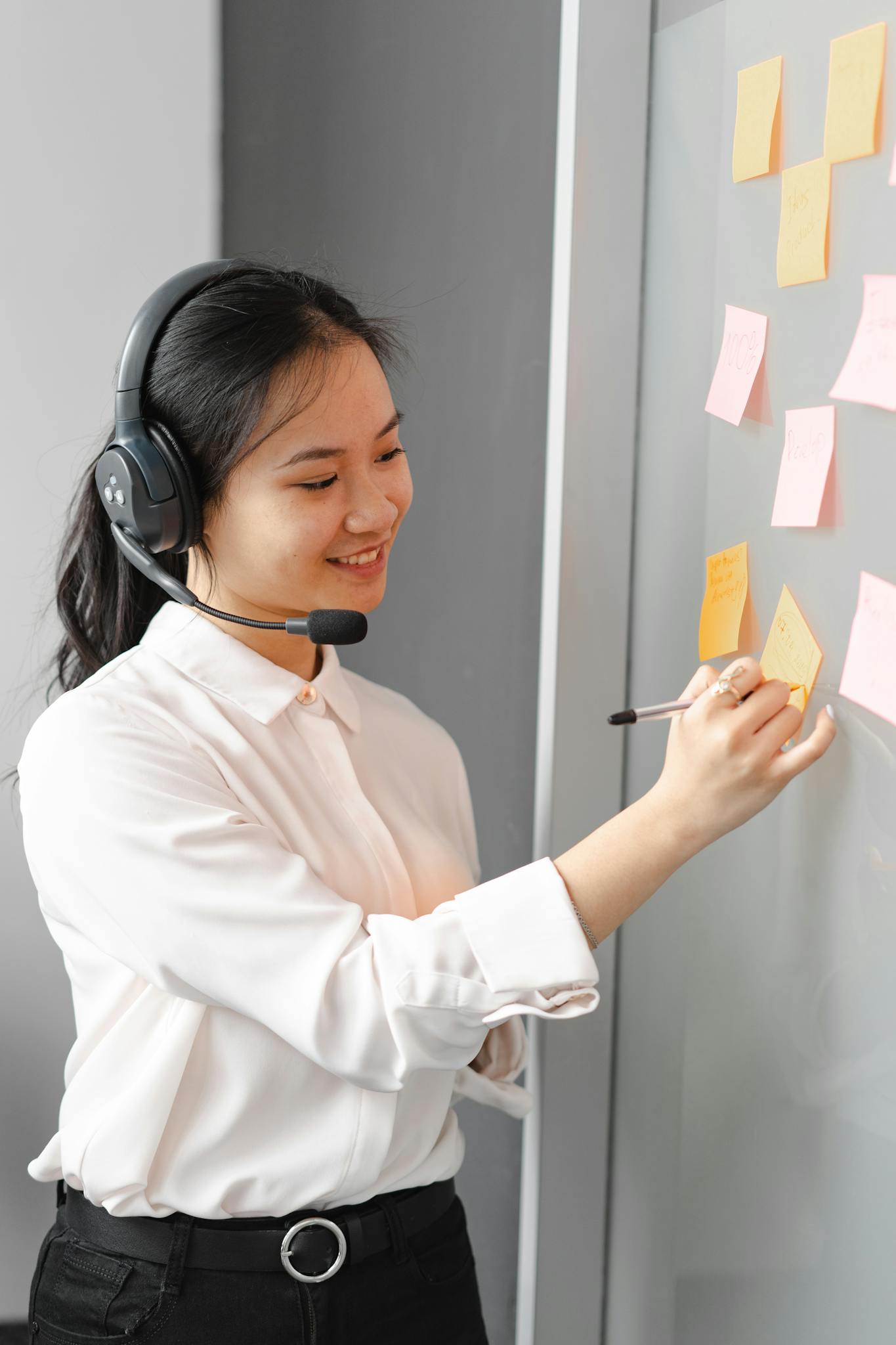 Smiling call center agent wearing headset, writing notes in office.