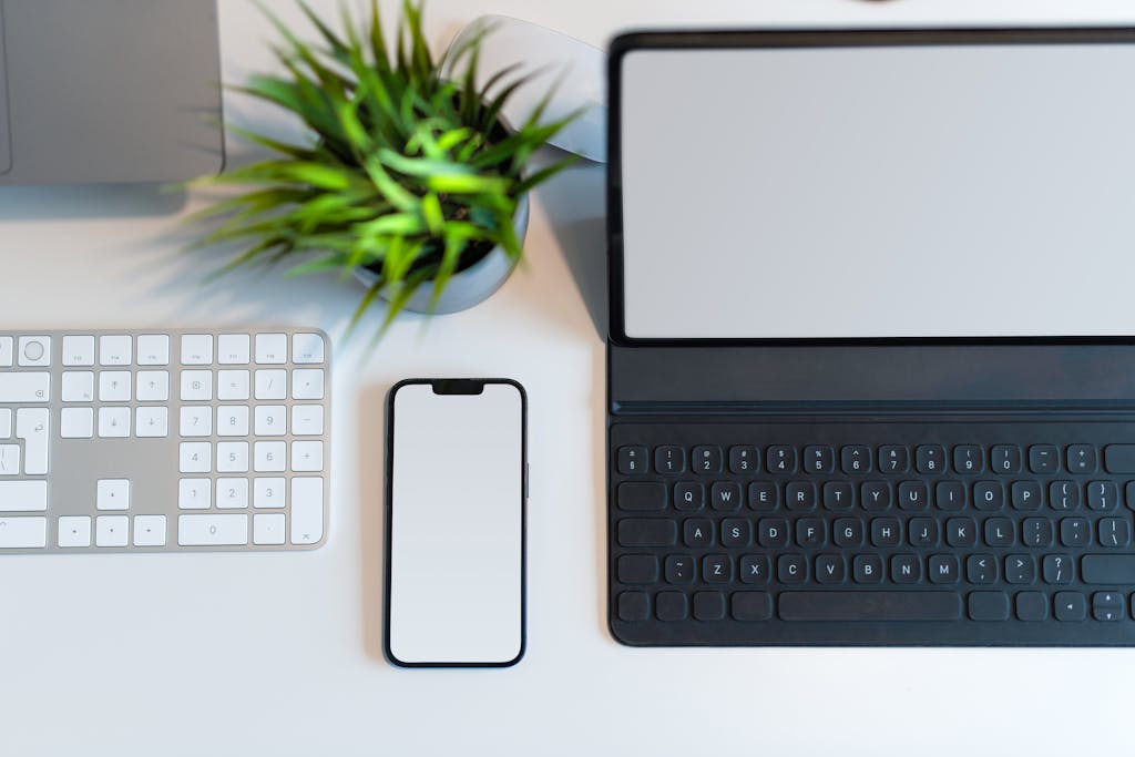 Top-down view of a modern workspace with a laptop, smartphone, keyboard, and plant.